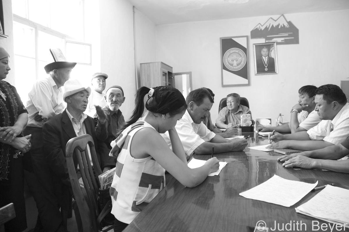 Sveral older and mid-aged men and one woman sitting around a table signing papers in Kyrgyzstan.